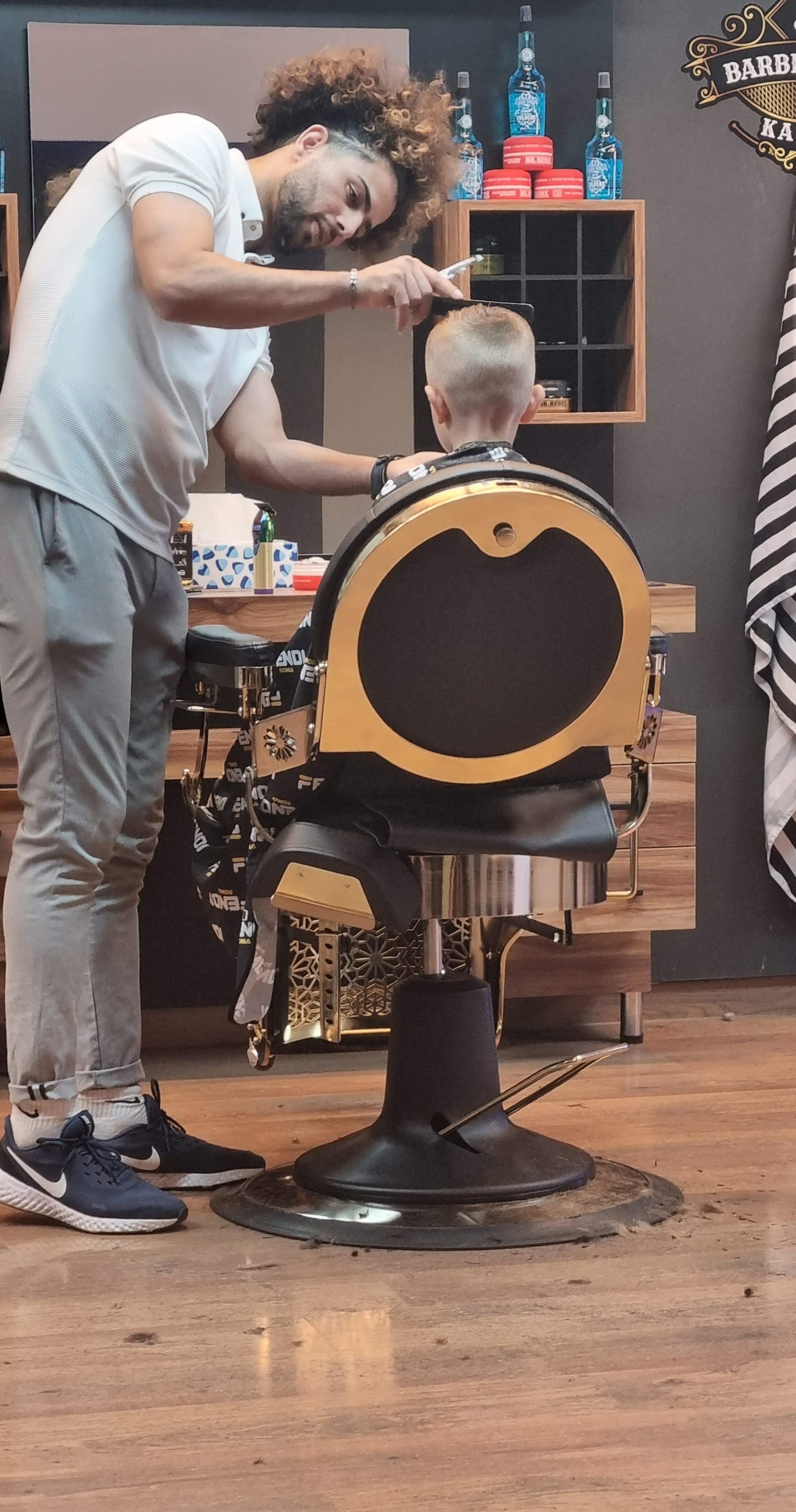 Een barbier knipt een jongen in de zwart-gouden barbierstoel, met de houten wand en spiegels erachter